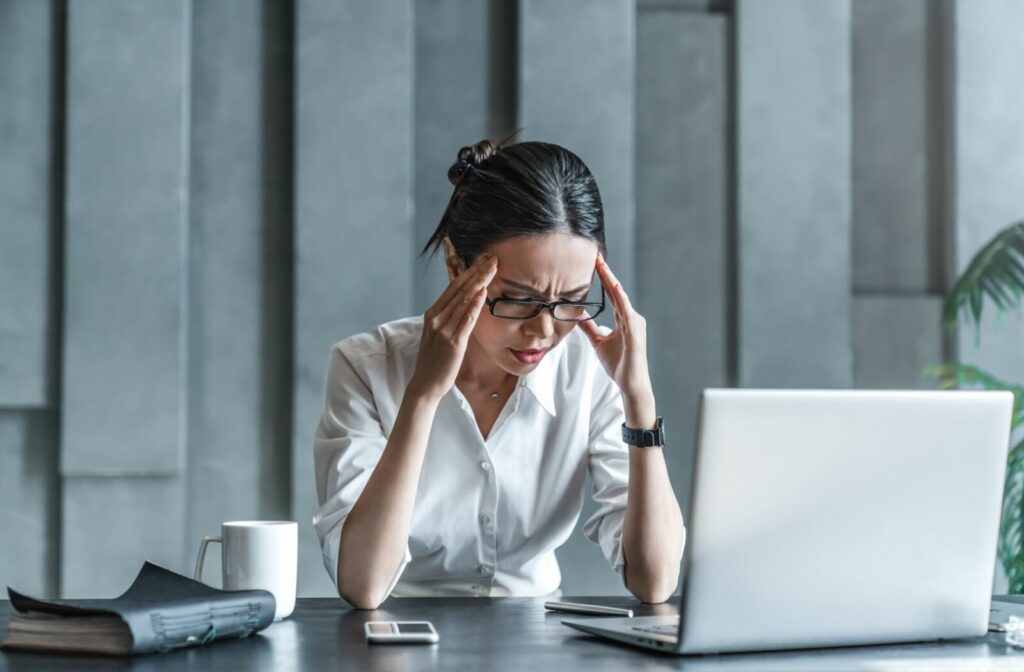 An adult rubs their temples as a tension headache sets in after hours on their computer.