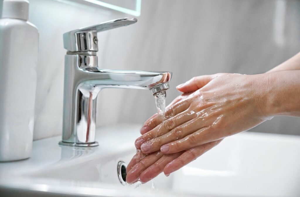 Hands being washed under a faucet in a bathroom sink.