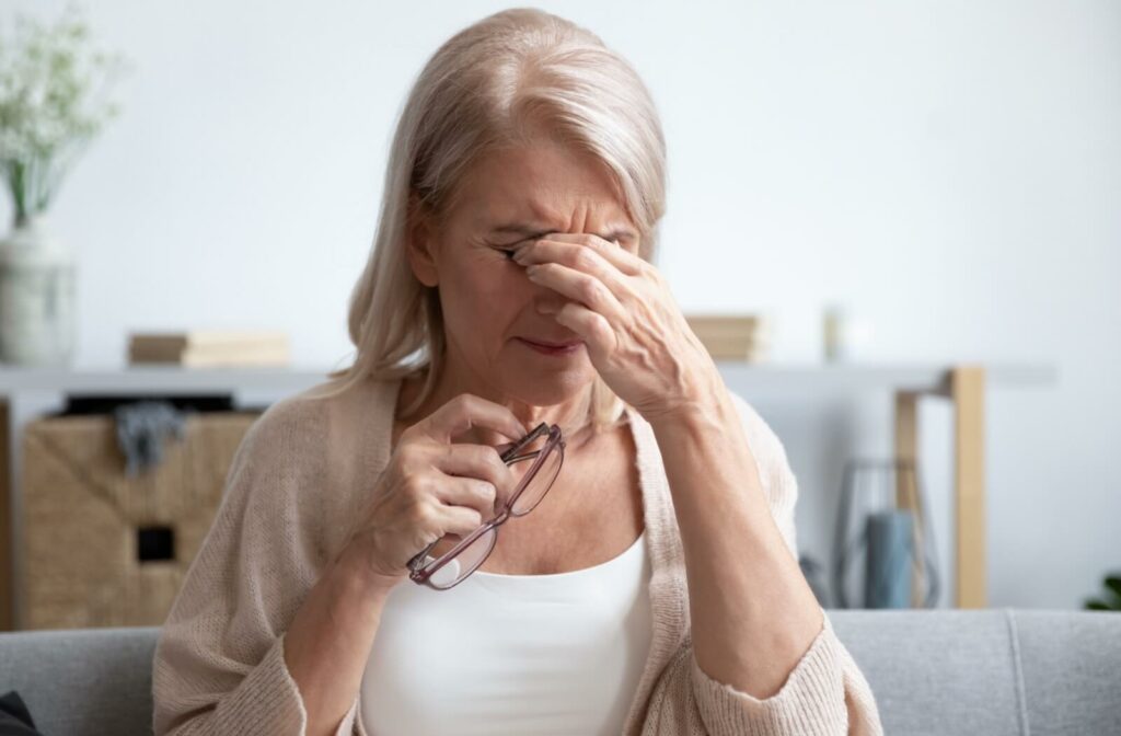 Older adult squeezing and rubbing eyes while holding glasses in other hand.