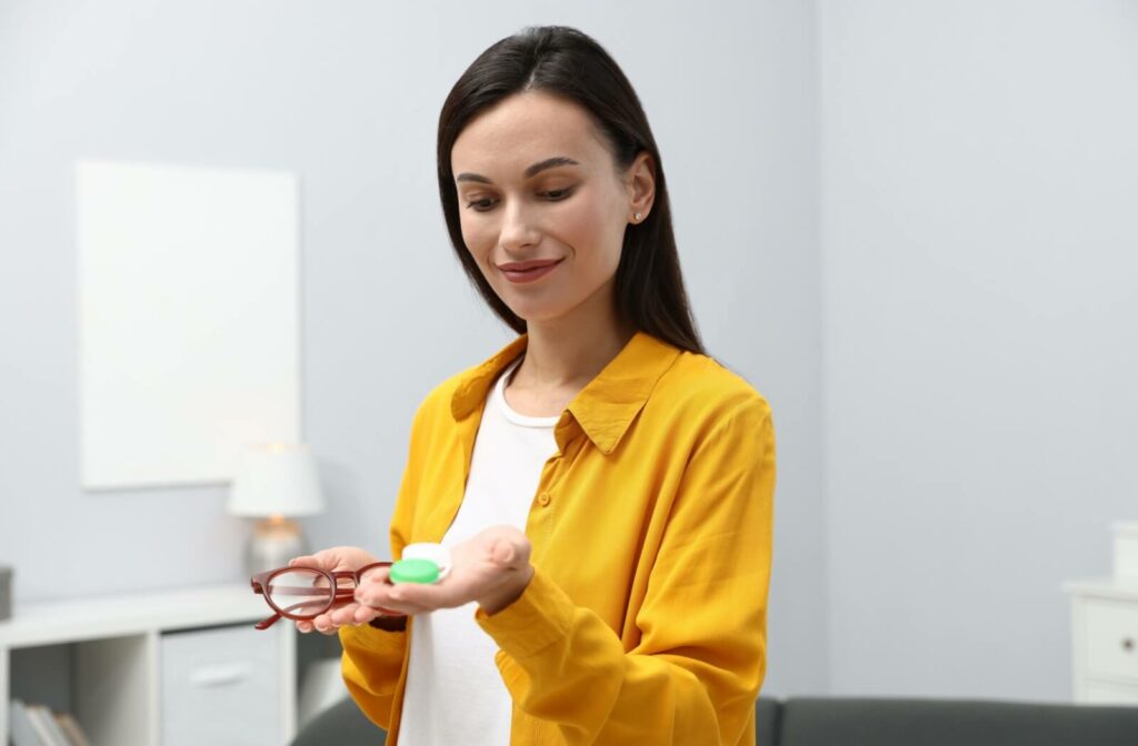 Person holding eyeglasses and a contact lens case, comparing vision correction options.