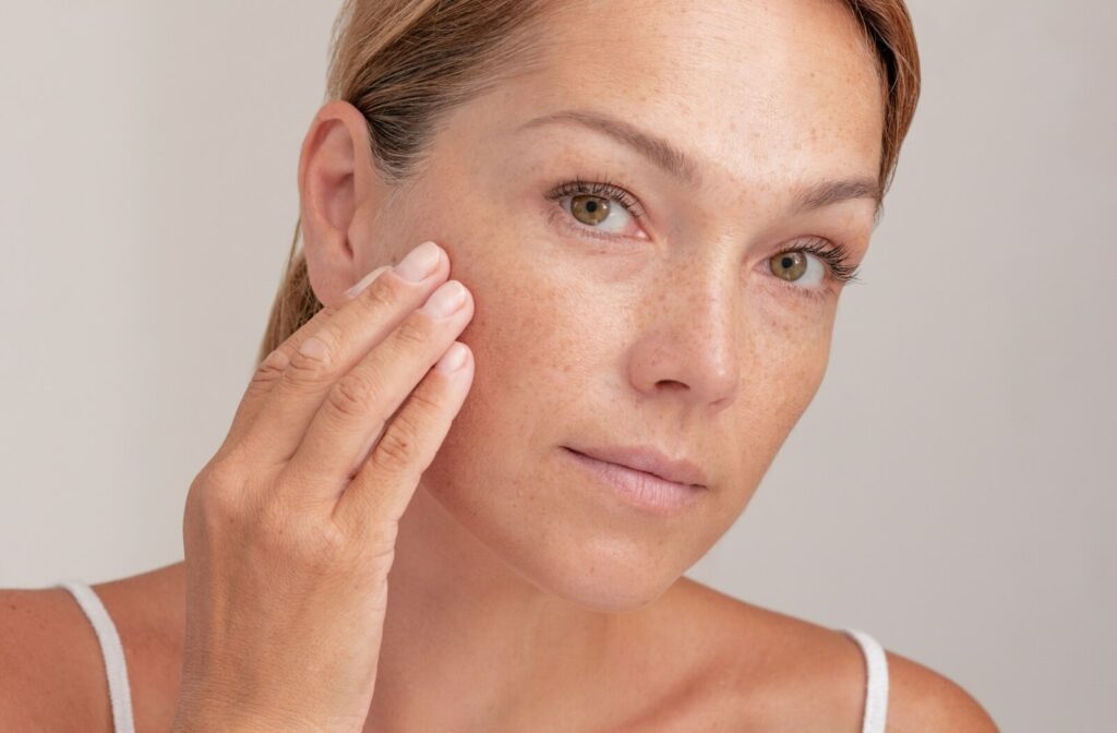Close-up of an individual touching their cheek to show freckles and age spots.